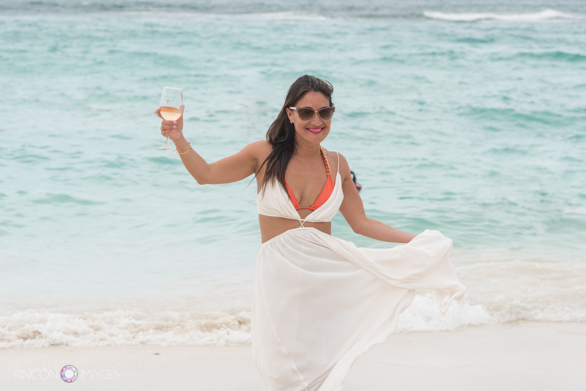 Bride wearing a white beach dress with an orange bikini holding a glass of white wine on the beach in St barths. 