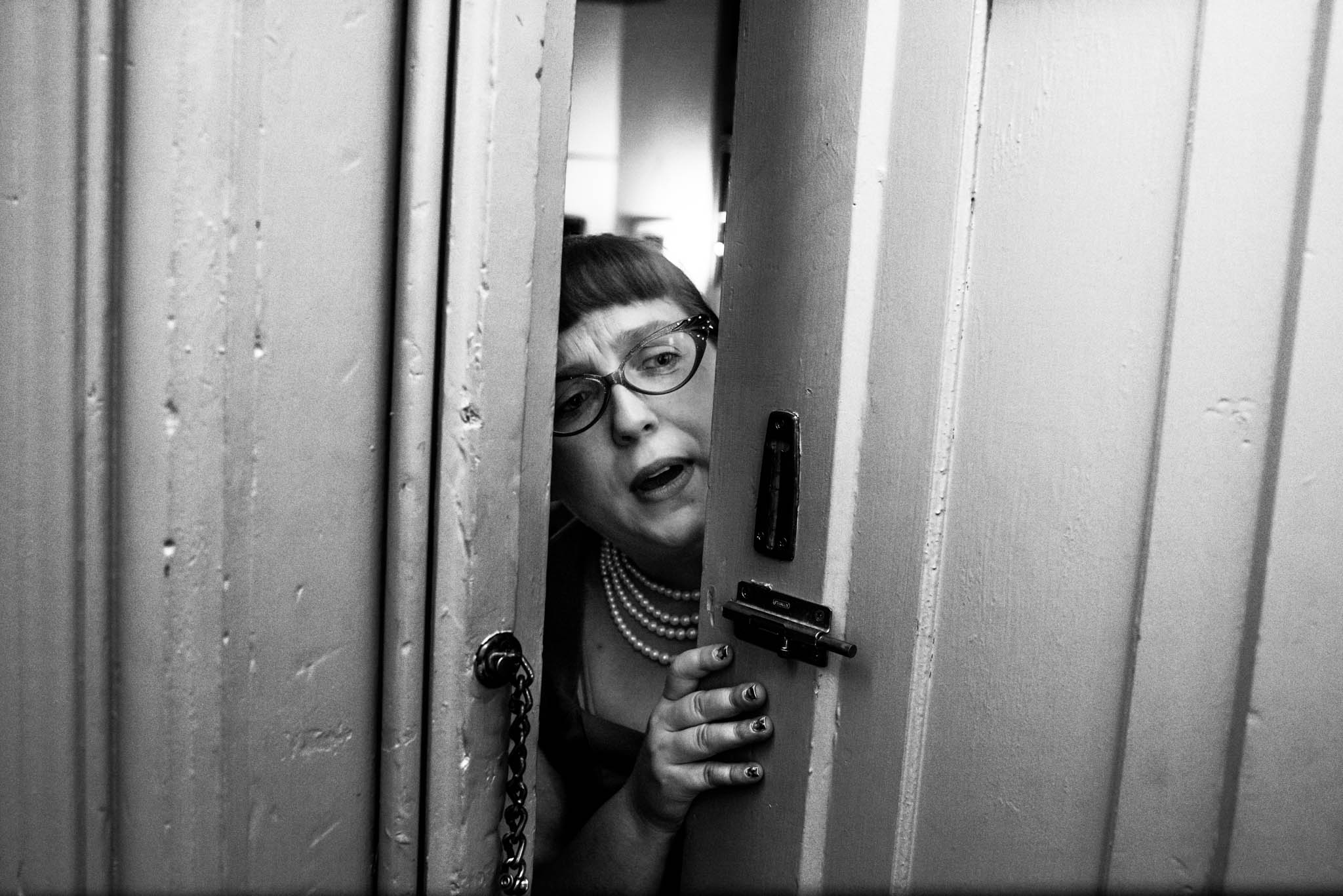 Black and white photo of woman peeking through door